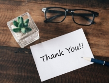a thank you note on a wood table next to a pair of glasses and a succulent