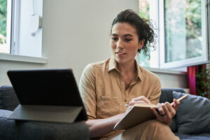 Waist up portrait view of the brunette female psychologist making notes with pleasure smile while holding video call with patient