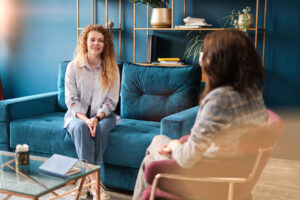 Happy red-haired woman talking to a female psychologist. Discusses her problems, mental trauma. Consultation in the office on the sofa. Positive mood.