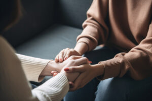 two women sitting on couches across from one another holding hands