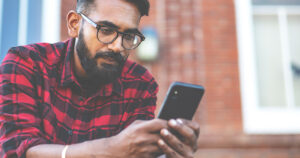 Man in red plaid shirt texting on phone