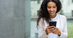 Woman in beige cardigan texting on phone