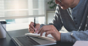 Person with laptop, writing in notebook