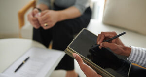 Hands of therapist using tablet while talking to patient