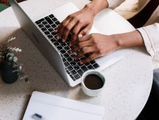 Hands typing on a laptop, next to coffee and plant