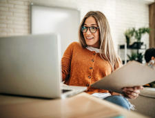 Woman holding clipboard while looking at laptop