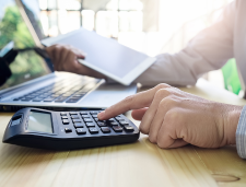 Person typing on calculator with laptop and tablet